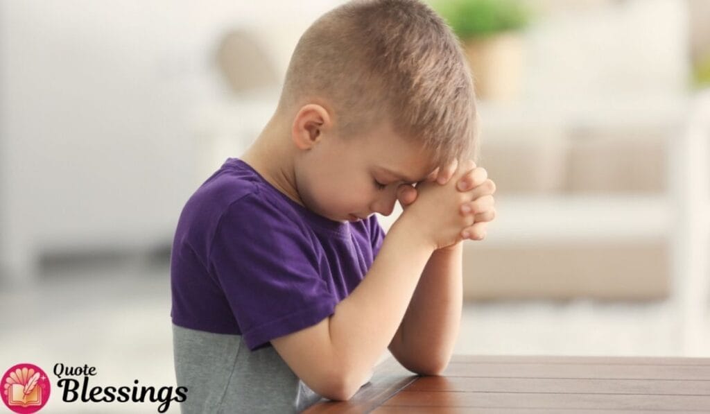 Young boy with closed eyes praying at a table in a peaceful indoor setting.
