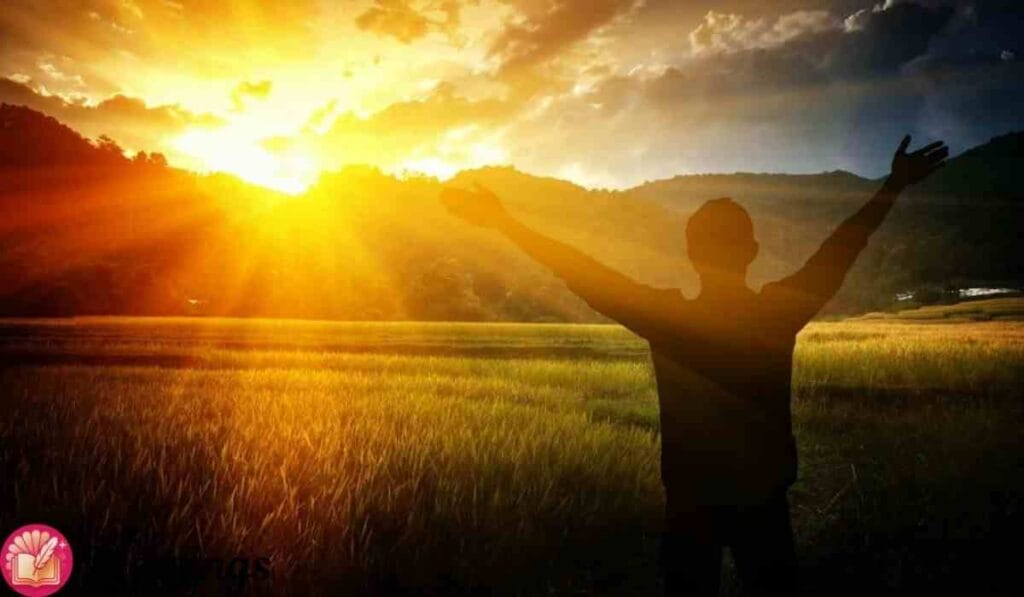 Man with raised arms in field at sunrise, facing mountains—symbol of morning prayer and gratitude.